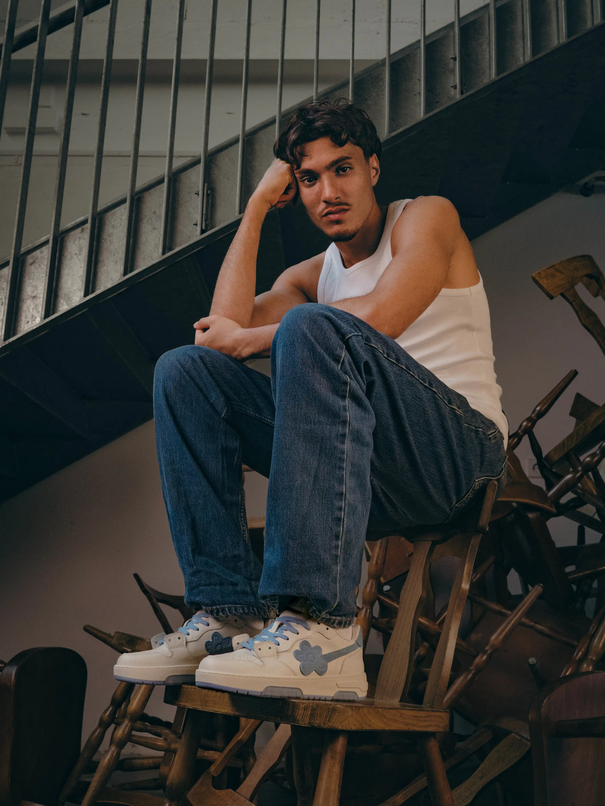 Flin Blue Bloom worn with blue jeans and a white tank top, on a model seated in a stairwell
